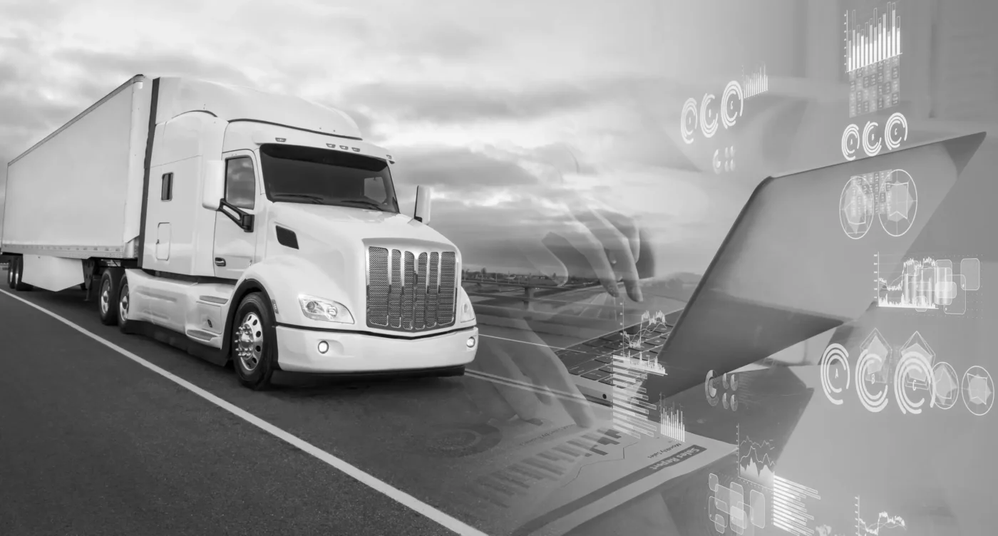 White and black photo of a truck driving on a road and hands typing on a laptop