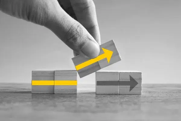 Black and white photo of a hand moving wooden cubes with arrows painted on them.