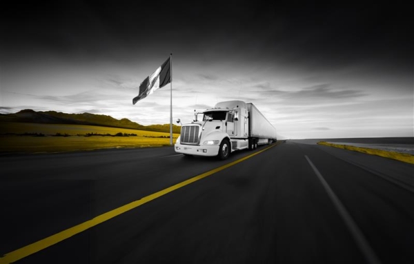 Transport truck driving on highway with Mexico flag on pole blowing in the wind on side of road.