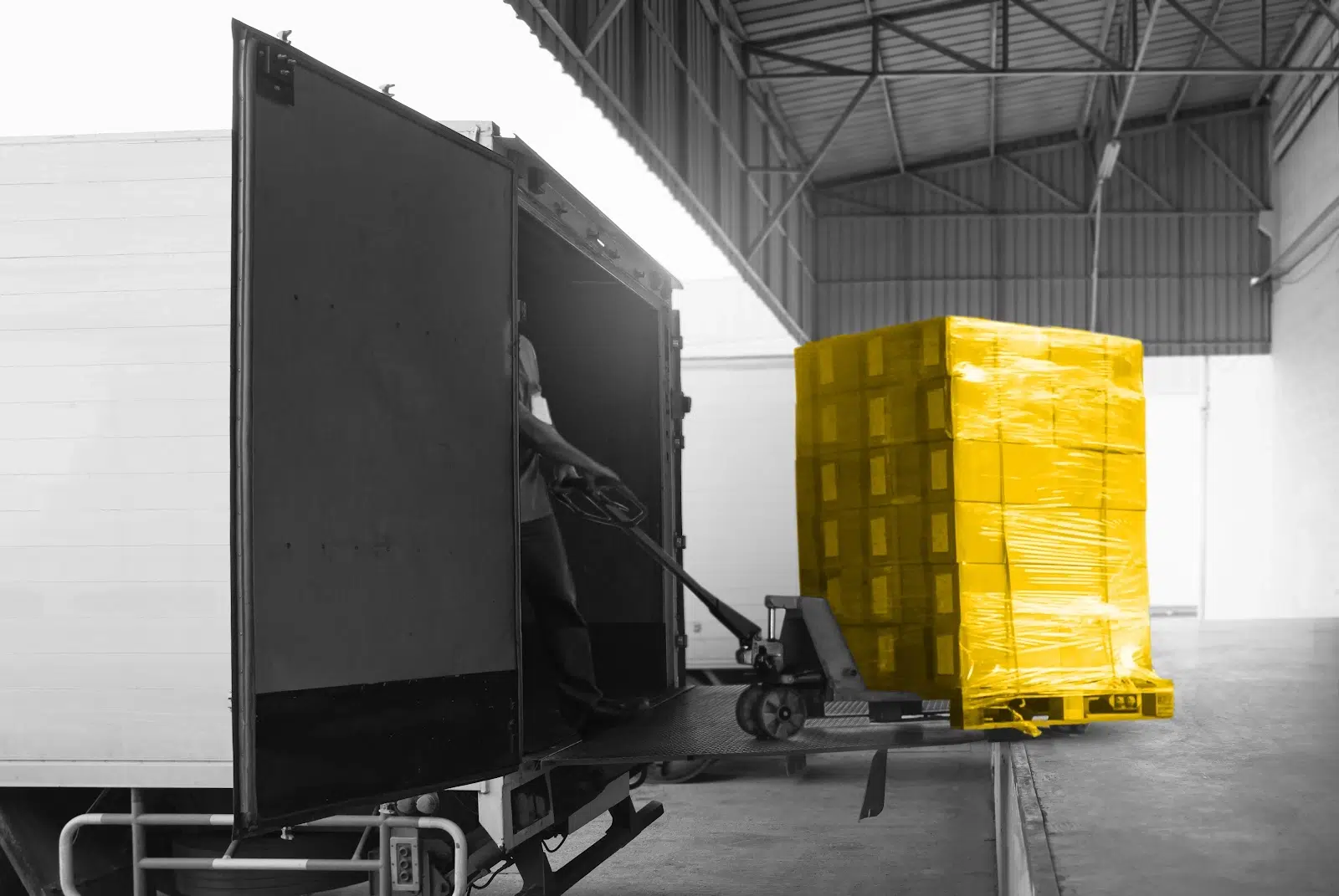 Black and white photo of pallets being loaded into a truck. Boxes colored yellow.