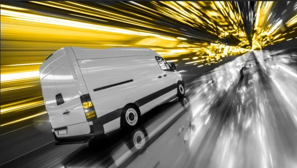 Black and white photo of a small truck driving through a tunnel. Tunnel lights colored yellow.