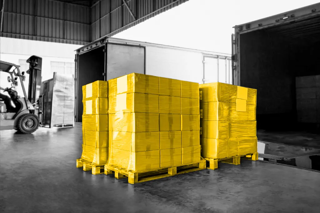 Black and white photo of pallets being loaded into a truck. Boxes colored yellow.