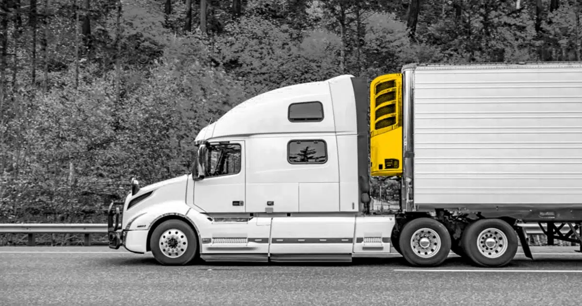 Black and white photo of a truck driving on a road. Truck cabin colored yellow.